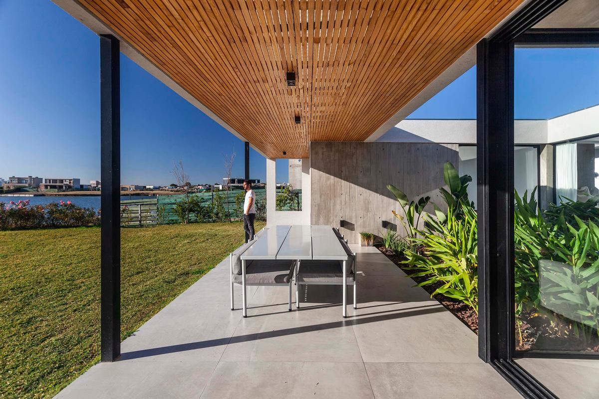 Área de jantar externa moderna com teto de ripas de madeira e vista costeira — projeto Casa H, por LSA., em Belén de Escobar