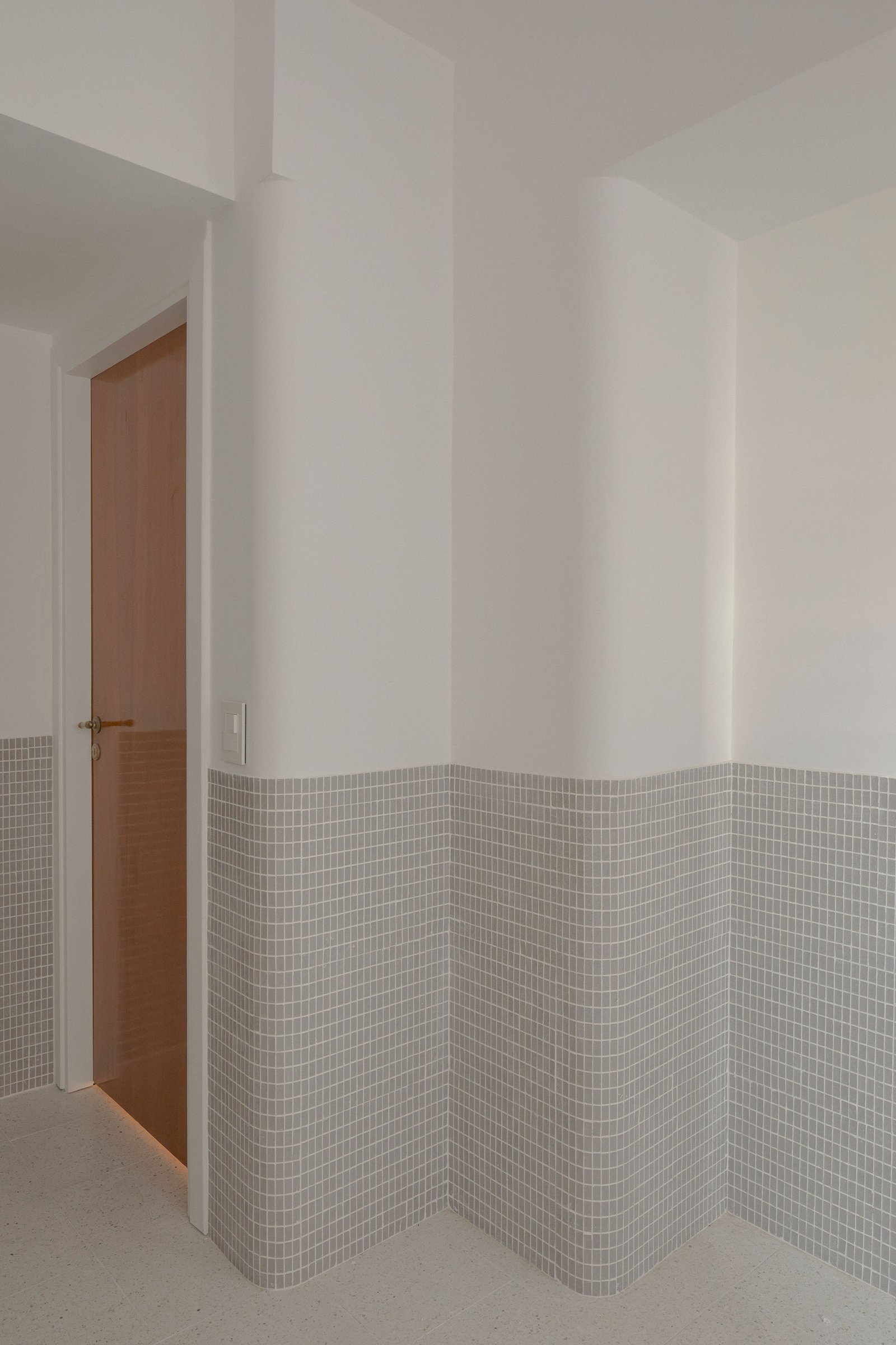 Corredor minimalista com parede curva de mosaicos cinzas — projeto Reforma O'Higgins, por Estudio YME, em Belgrano