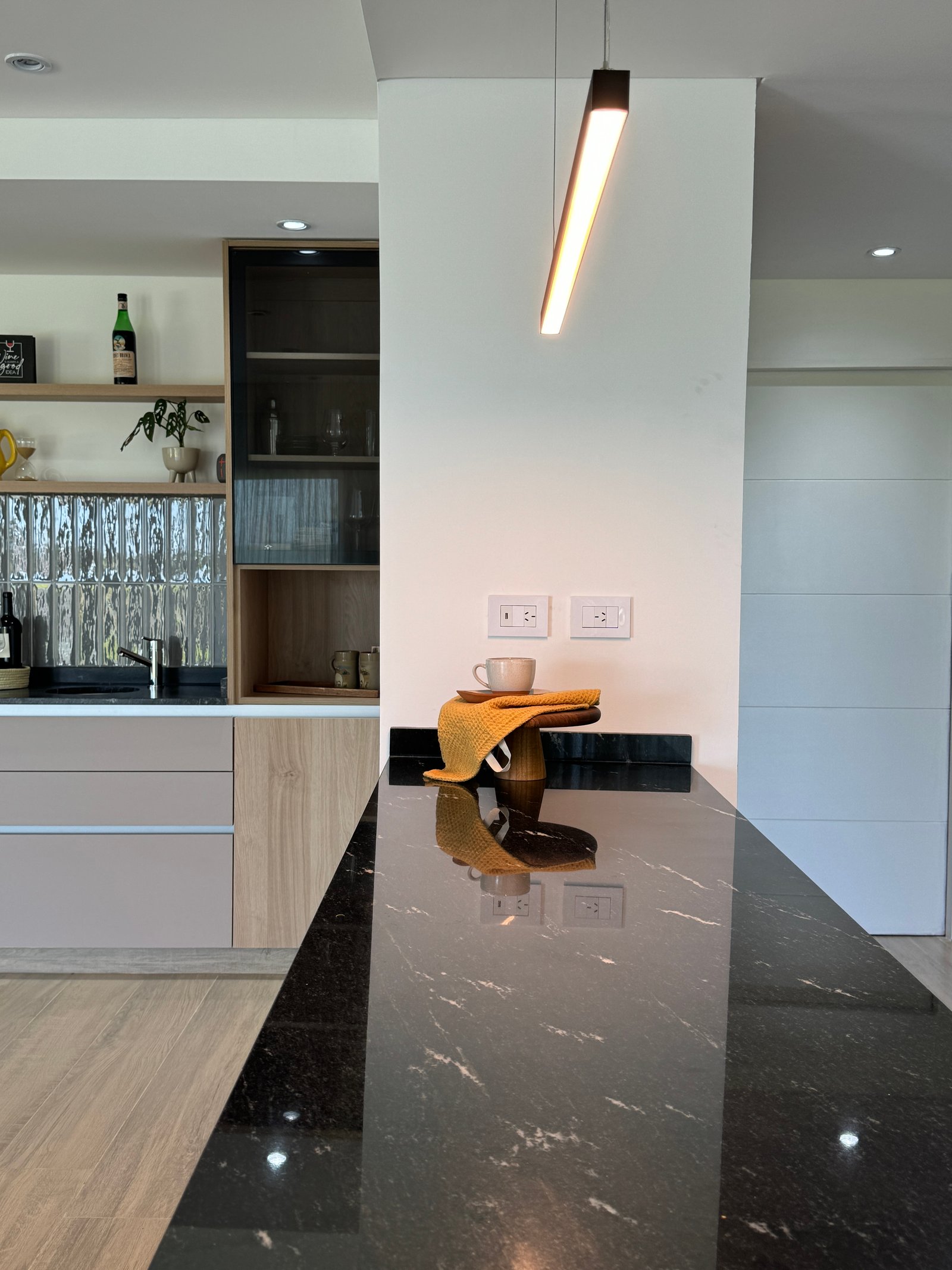 Cozinha moderna com bancada de mármore preto e luminária pendente longa — projeto San Simon II, por Estudio Stepa, em Canning