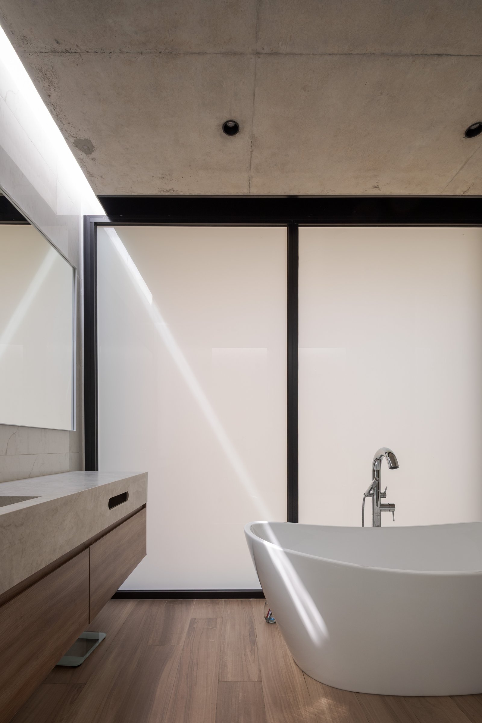 Baño moderno con techo de hormigón, luz natural y bañera exenta — proyecto Casa PLANALTO, por Grupo CRBN, en Av. Pres. Perón 10298