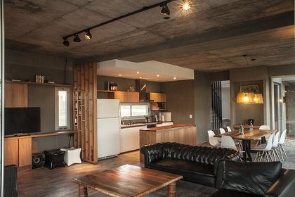 Living amplio con sofa negro, cocina integrada y techo de hormigon — proyecto Casa MM, por Facundo Arana Arquitecto