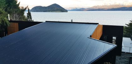 Fachada moderna con techo metálico corrugado y detalles en madera, vista al lago — proyecto Casa Península San Pedro, por Servente Larrazabal Arq, en Bariloche
