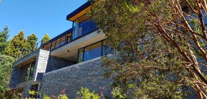 Fachada moderna multinivel con revestimiento de piedra y concreto — proyecto Casa Península San Pedro, por Servente Larrazabal Arq, en Bariloche