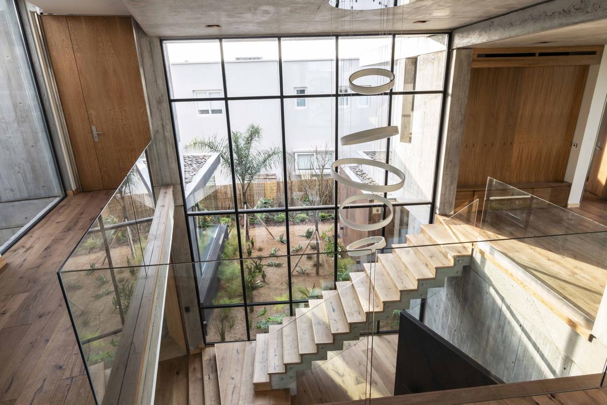 Átrio moderno de pé-direito duplo com escada flutuante e jardim interno — projeto Casa CZ, por Estudio Juan Trivelloni