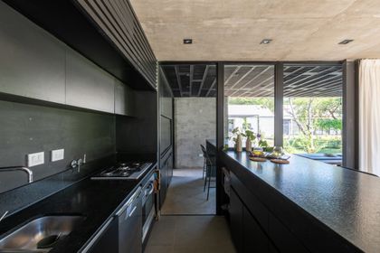 Cocina moderna negra con isla, ventanales hacia jardin exterior — proyecto Casa SI, por Grupo Studio, en Villa Allende
