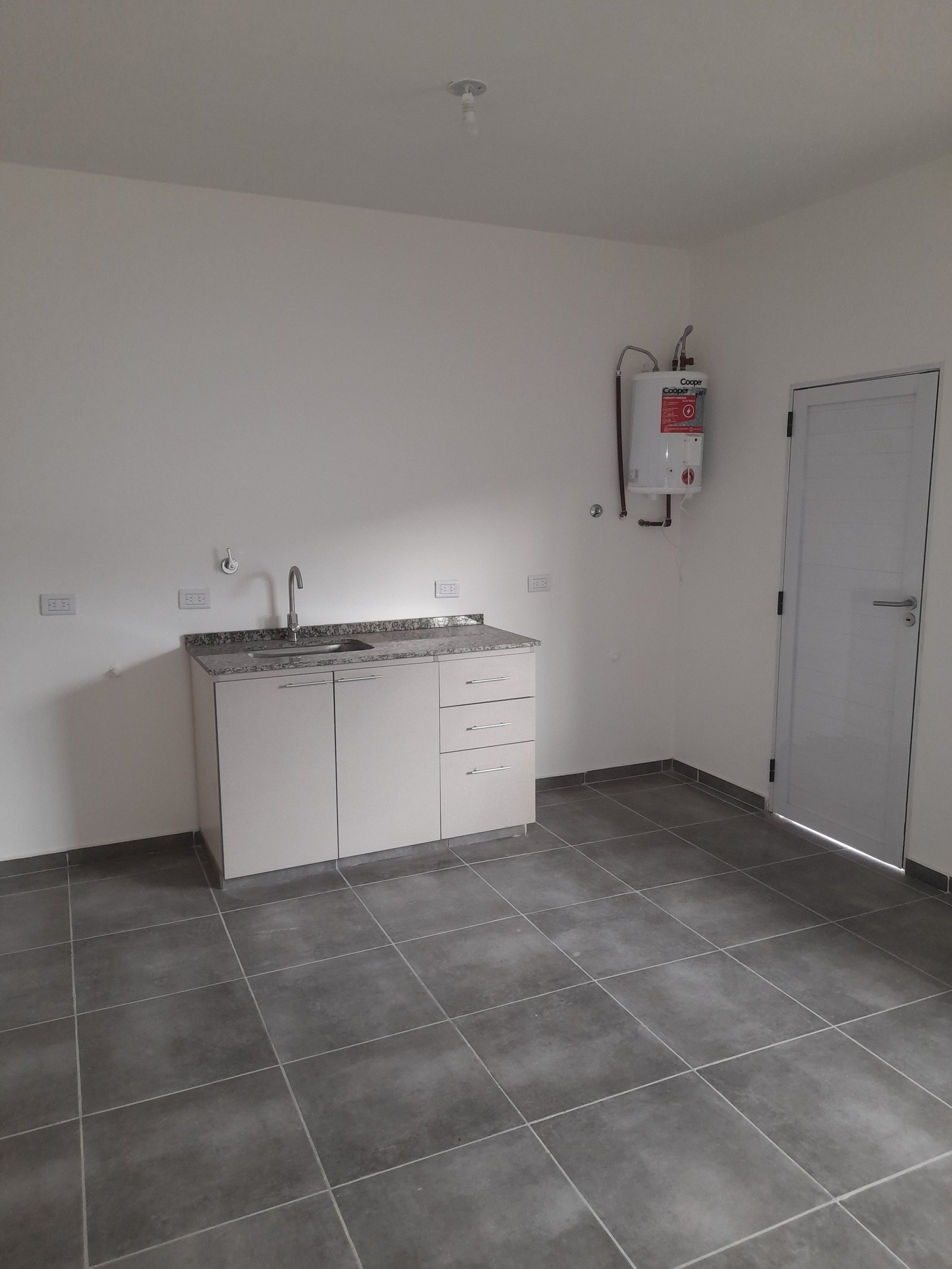 Cocina pequeña, gabinetes blancos, mesada de piedra y piso de cerámica gris — proyecto Departamentos, por CN Construcciones, en Alta Gracia