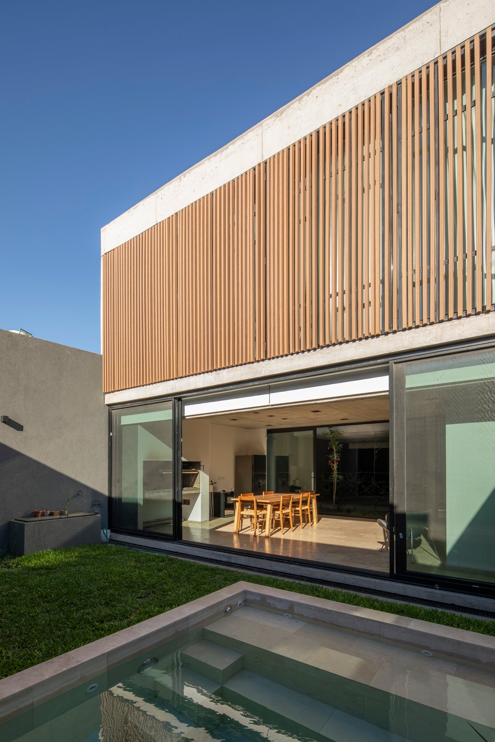 Fachada moderna con revestimiento de madera y piscina integrada — proyecto Casa MECHA, por Grupo CRBN, en B1712 Castelar