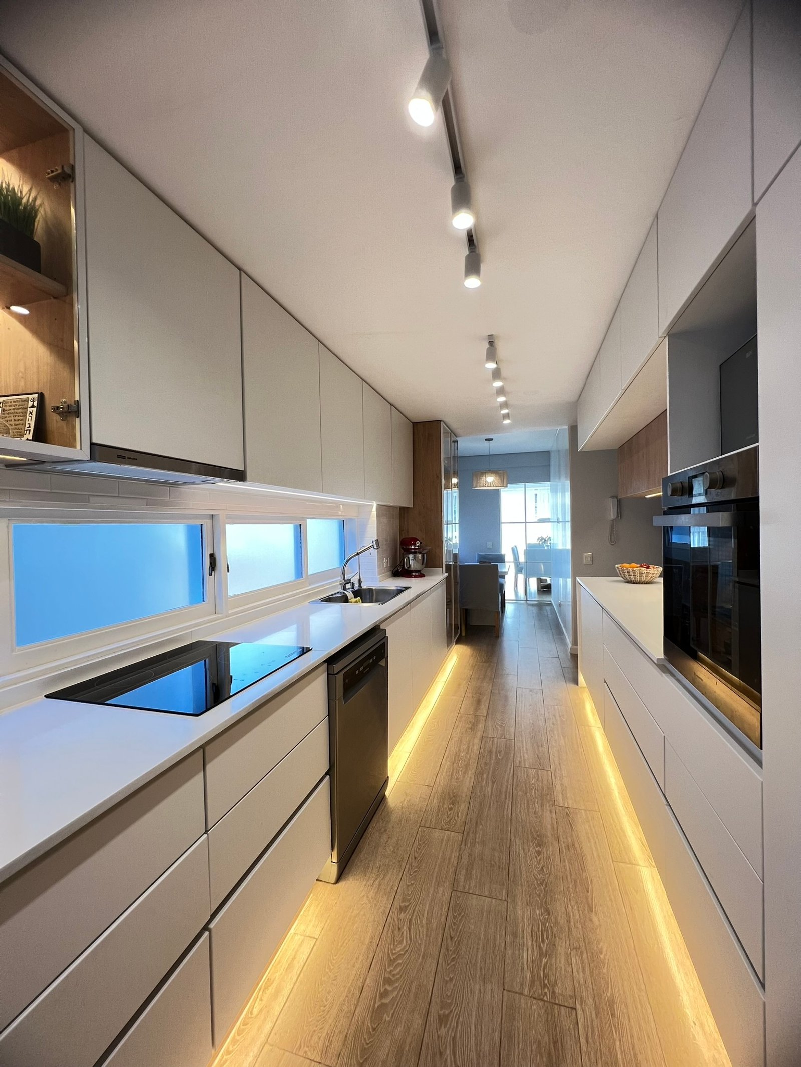 Cocina lineal moderna con gabinetes blancos y luz indirecta — proyecto Araoz, por MDBK Arquitectura, en Palermo