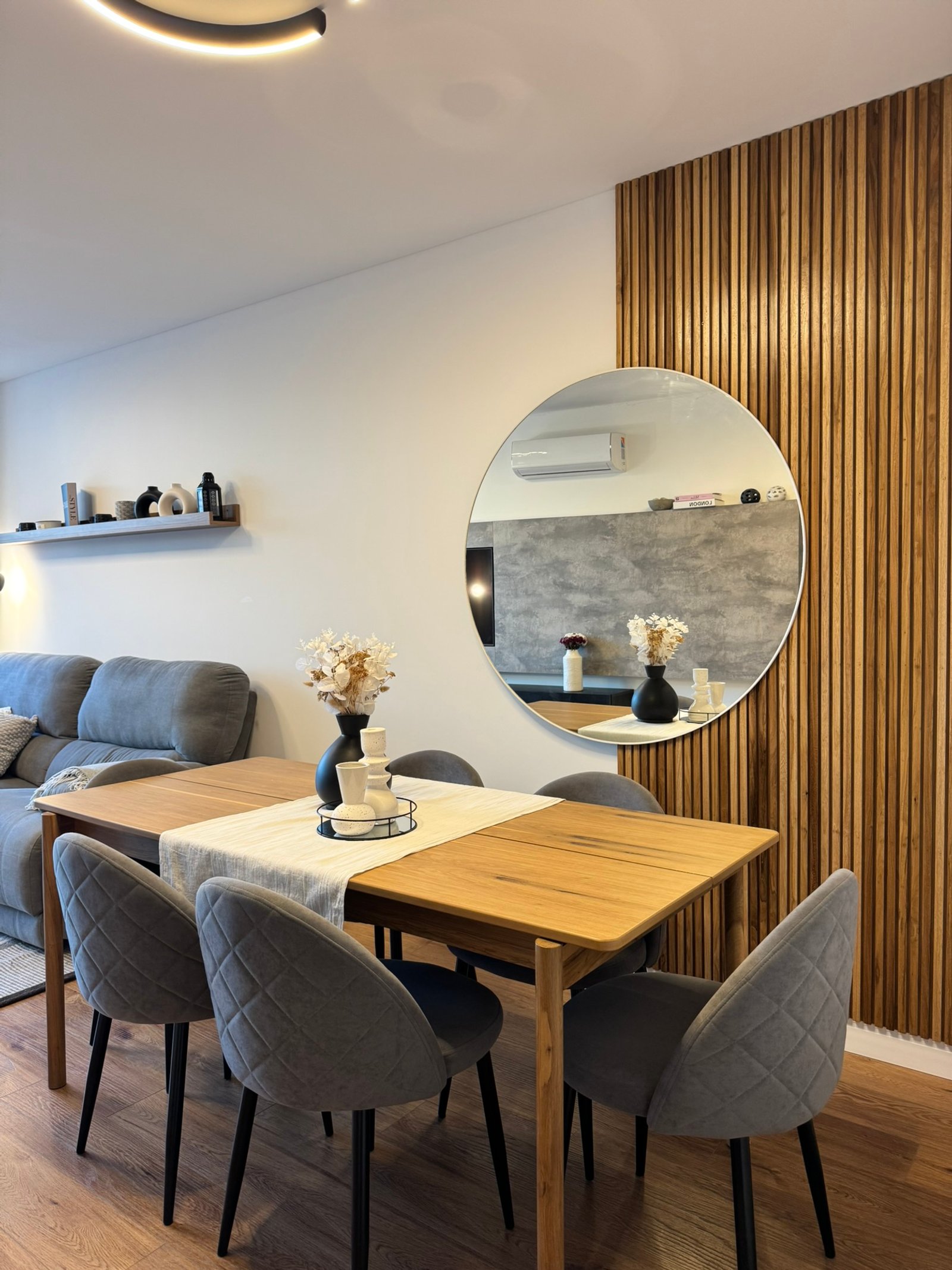 Sala de jantar escandinava moderna com parede de ripas de madeira e espelho redondo — projeto Ciudad de la Paz, por MDBK Arquitectura, em Belgrano