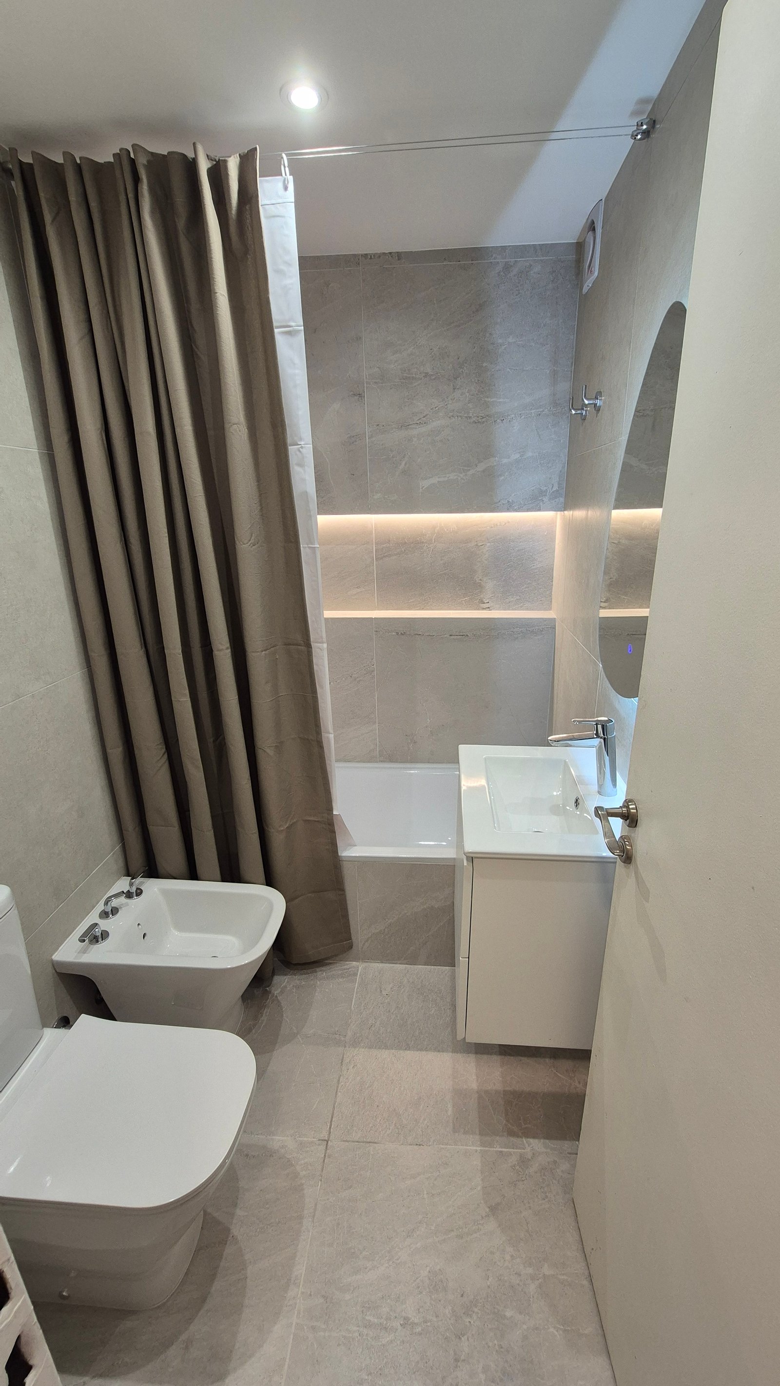 Baño moderno con cortina beige, bañera blanca y ducha oculta — proyecto 26-001 Larrea, por RenovArqui, en Larrea 1252