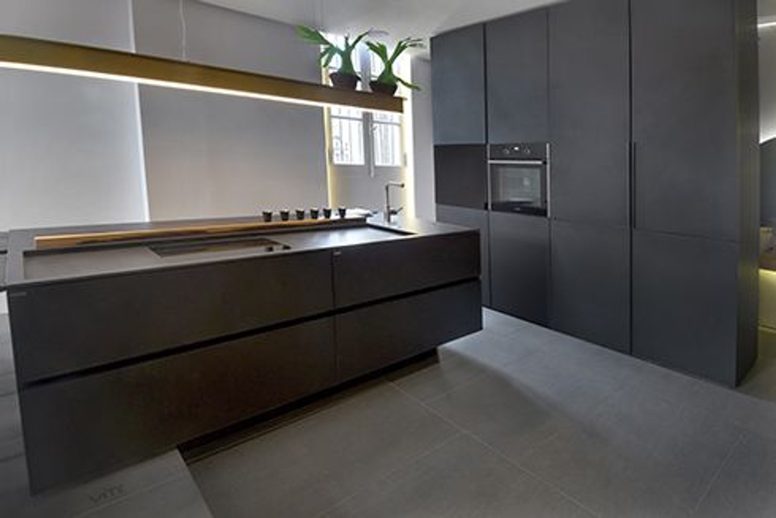 Cocina moderna con isla oscura monolítica y artefacto lineal dorado — proyecto Casa Foa Devoto 2018, por Vite Porcellanato, en Buenos Aires