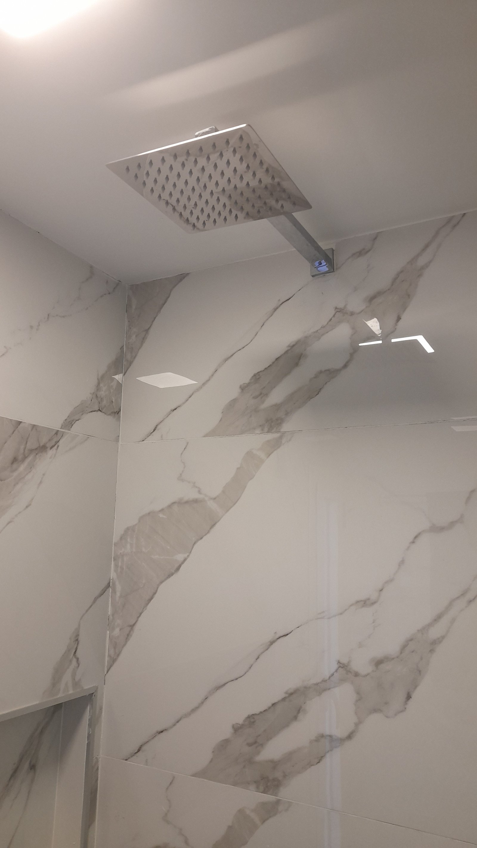 Banheiro moderno com chuveiro quadrado, azulejos de mármore e luz indireta — projeto Remodelación de baño, por CN Construcciones, em Alta Gracia
