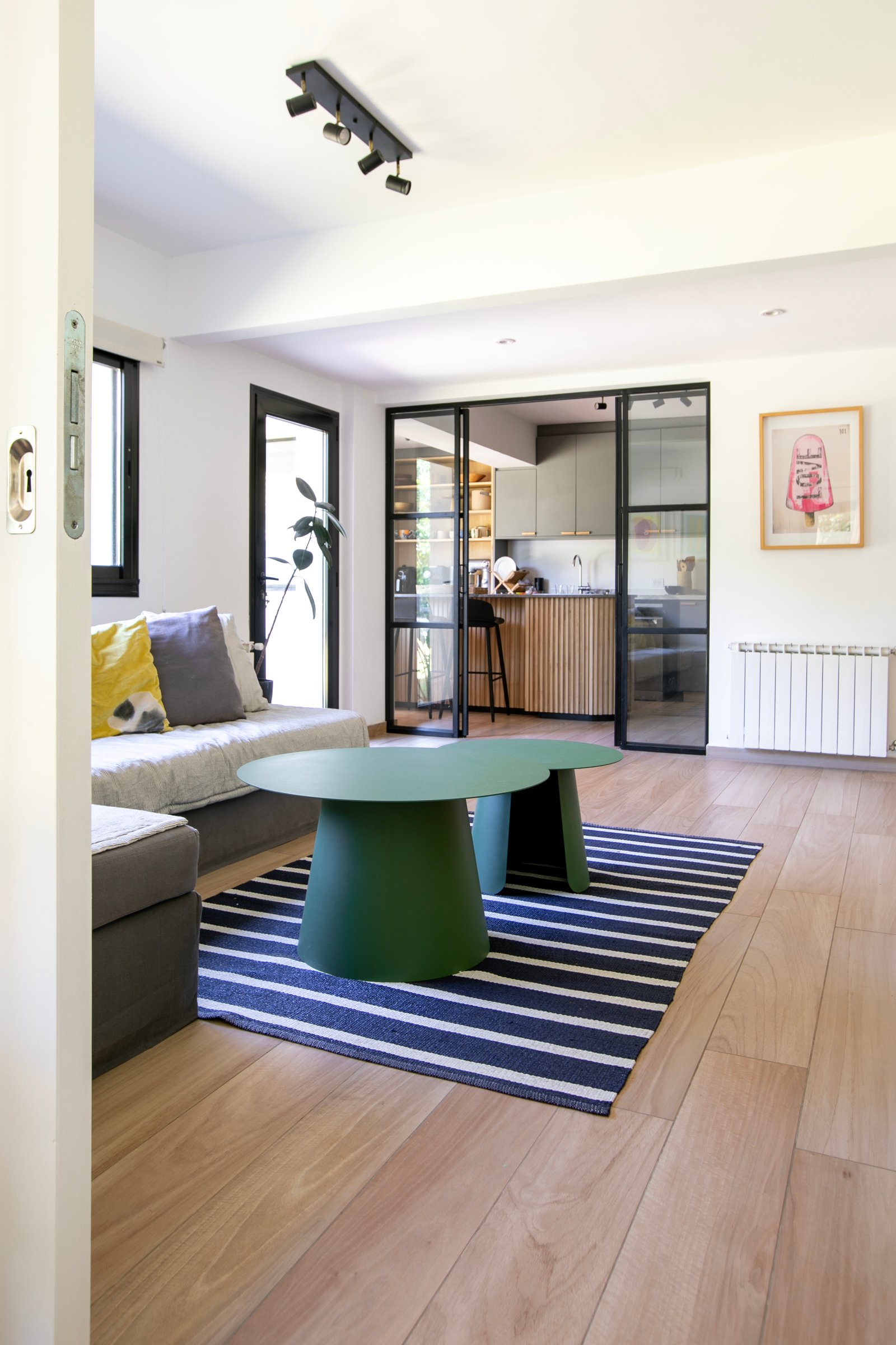 Living con cocina integrada, mesa verde escultural y alfombra rayada — proyecto PROYECTO CAT COURREGES, por ILVA, en Provincia de Buenos Aires