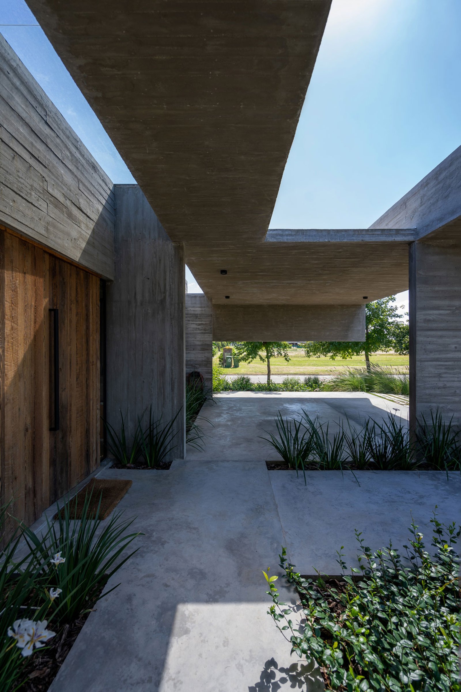 Fachada moderna de hormigón con amplias losas y vegetación integrada — proyecto Casa Tres Patios, por Besonías Almeida arquitectos, en Pilar