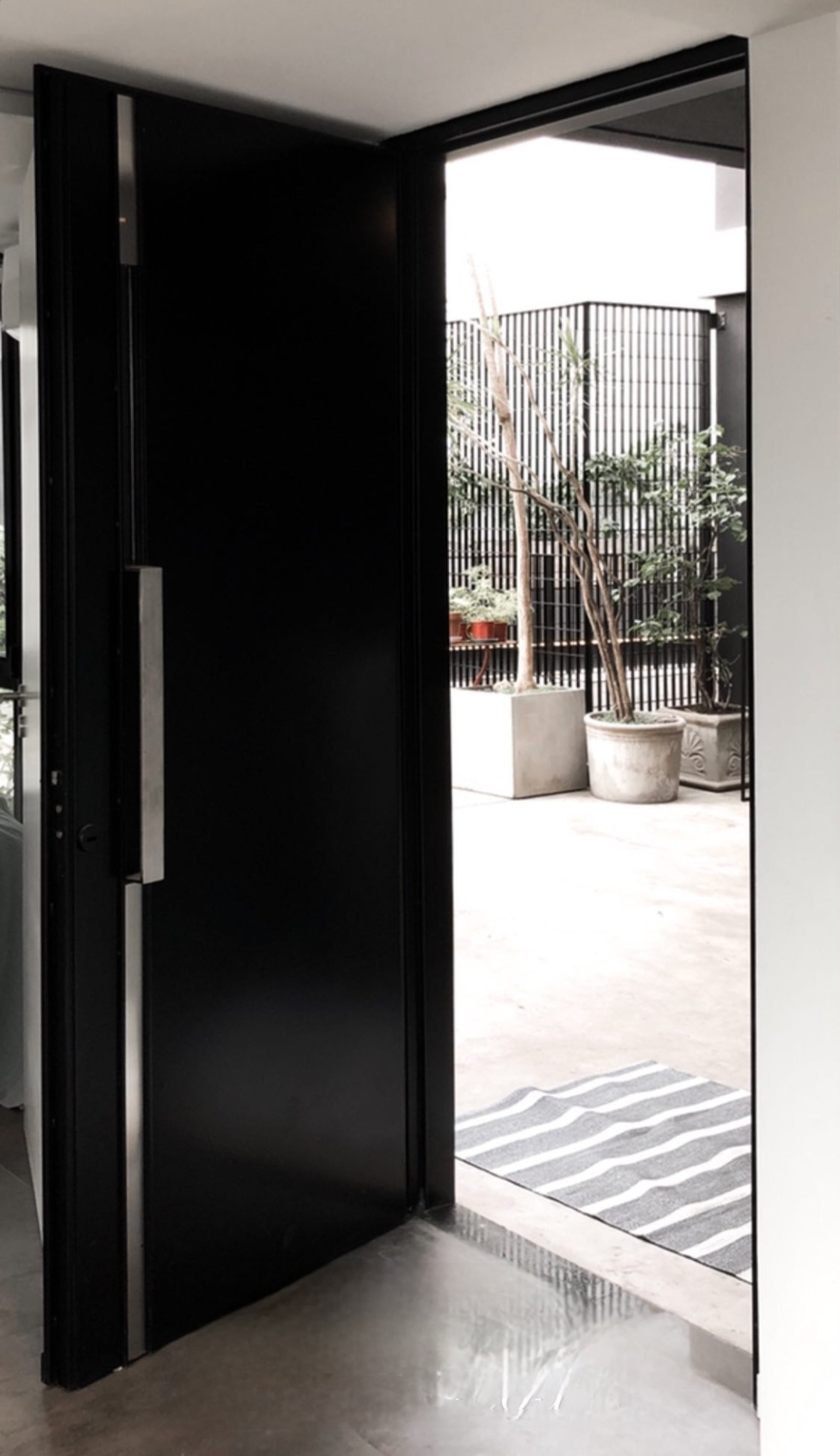 Fachada moderna con puerta pivotante negra y jardineras de hormigón — proyecto Teodoro, por Claraboia , en Belgrano R
