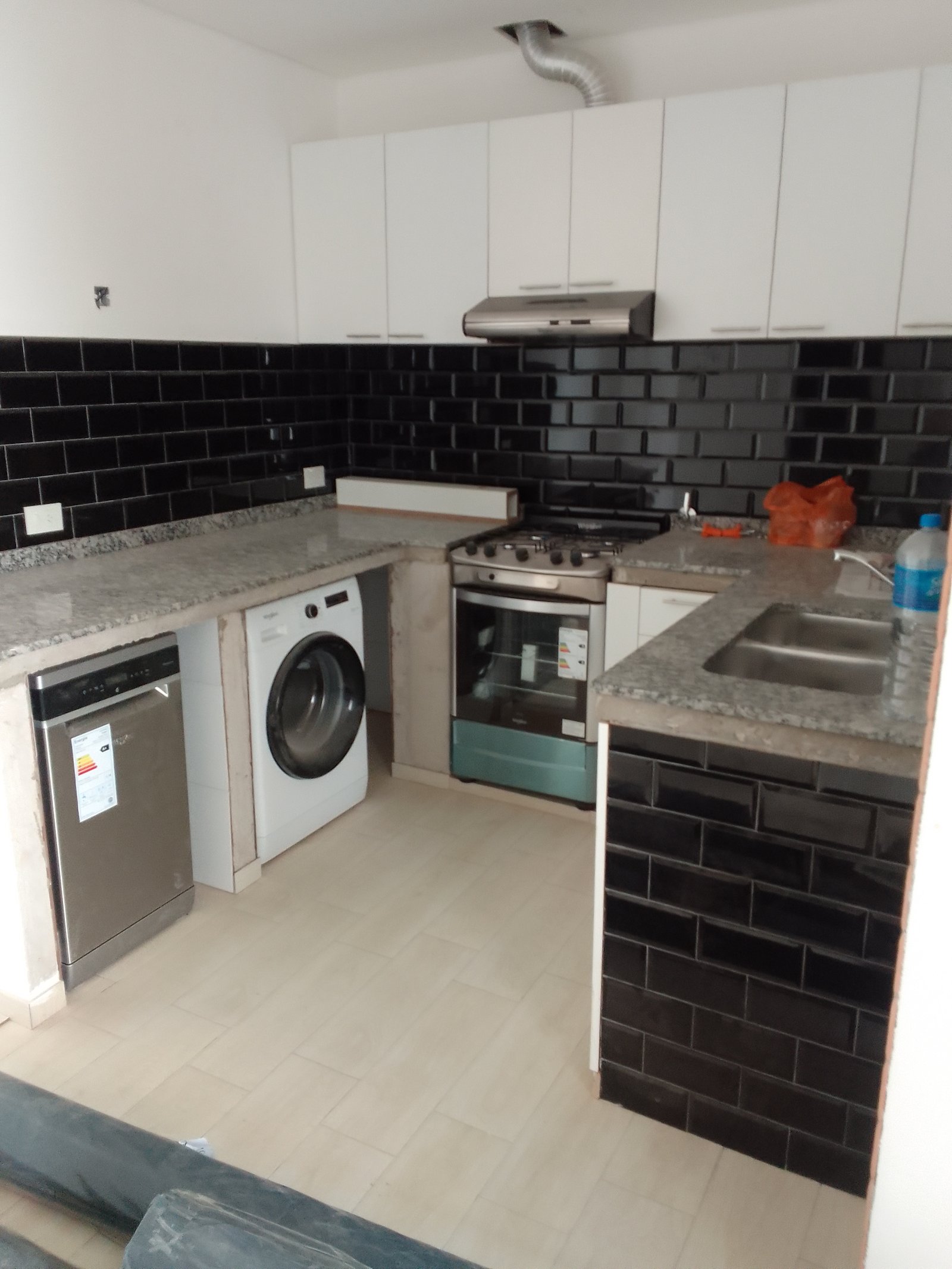 Cozinha moderna com azulejos pretos, armários brancos e eletrodomésticos de aço inoxidável — projeto Drogueria en Avellaneda, por Arquitecto Guido Niccoli, em B1872 Sarandí