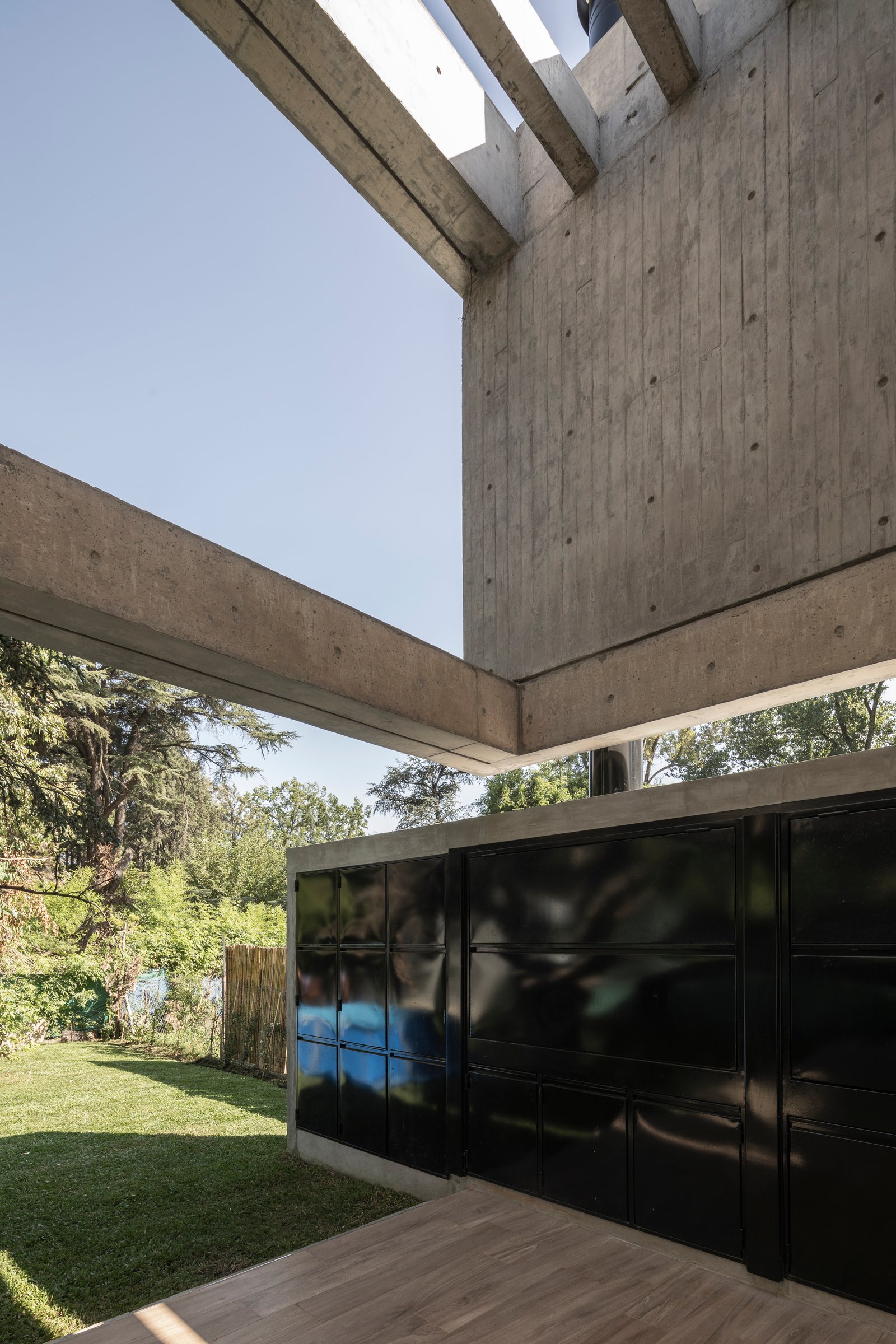 fachada moderna de concreto com portões pretos e jardim — projeto Casa Emilia, por Grupo CRBN, em Parque Leloir