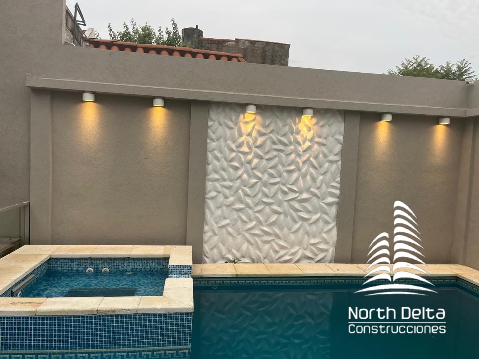 Área de piscina moderna com parede texturizada e iluminação integrada — projeto Construcción de Piscina+ Jacuzzi, por North Delta Construcciones, em El Palomar
