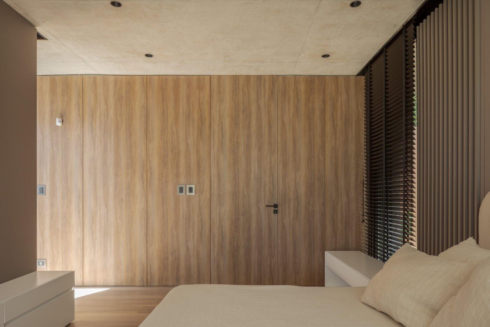 Quarto moderno com painéis de madeira natural e armazenamento embutido — projeto Casa PLANALTO, por Grupo CRBN, em Av. Pres. Perón 10298