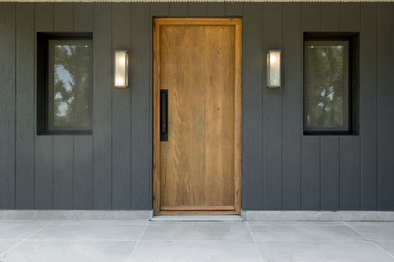 Fachada moderna con puerta de madera alta y ventanas a los lados — proyecto CASA AUGUSTUS NATURALE, por ILVA, en Provincia de Buenos Aires