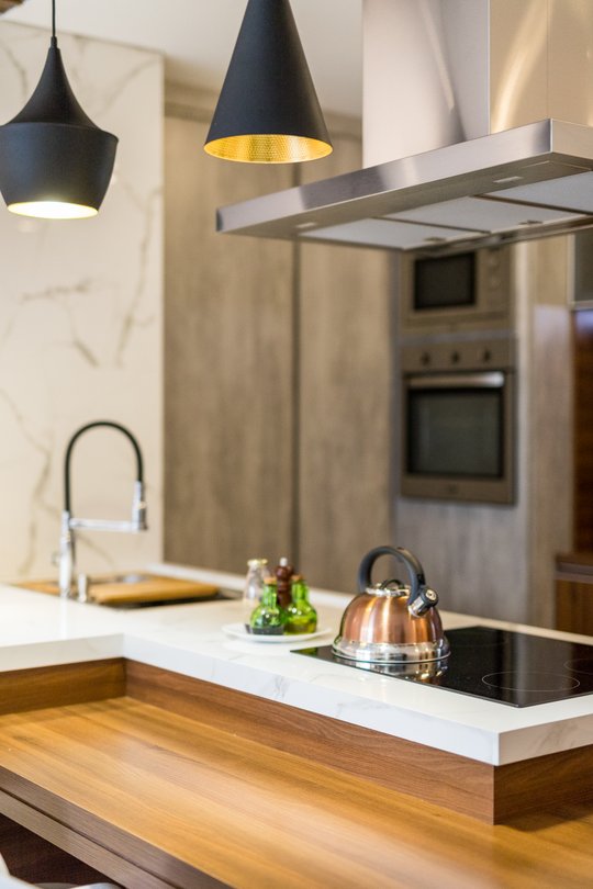 Cocina moderna con isla, mesada blanca y lámparas colgantes negras — proyecto Apto Sérgio e Lizandra, por Coletivo Arquitetura