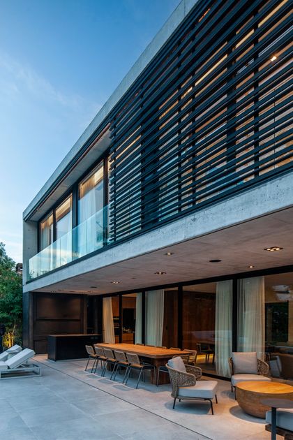 Fachada moderna con detalles en madera y hormigón, patio con comedor exterior — proyecto CASA AH, por GMARQ, en Garin