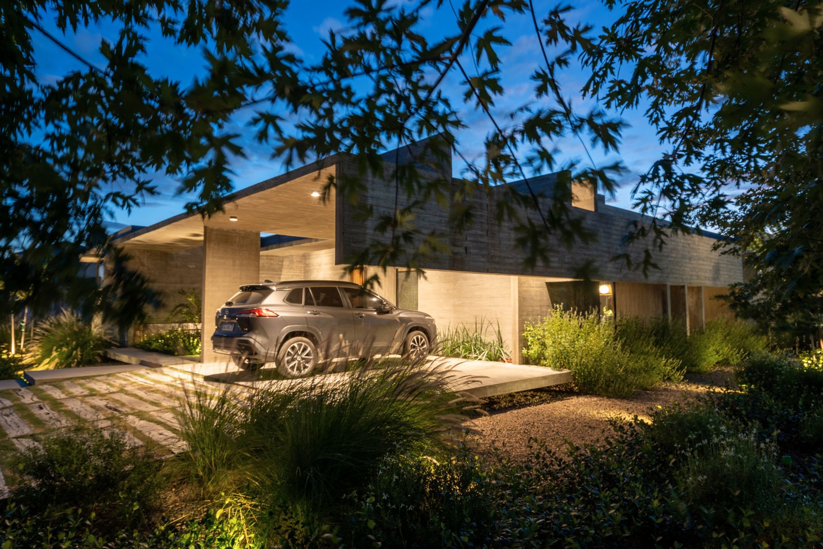 Fachada moderna de noche con vegetación exuberante — proyecto Casa Tres Patios, por Besonías Almeida arquitectos, en Pilar