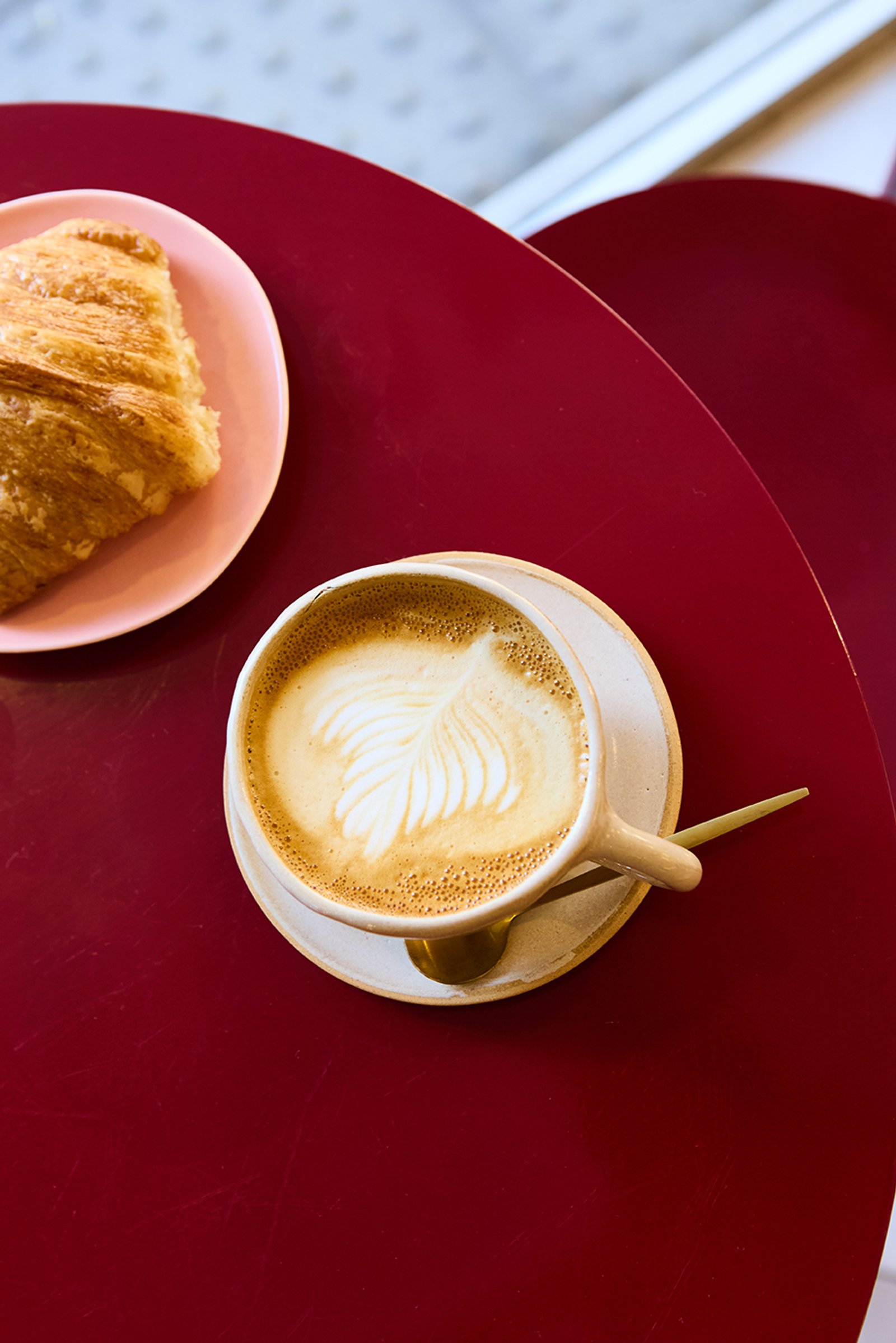 Mesa bordó con café con arte latte y croissant — proyecto Severina, por Estudio Plats, en Acoyte 1396