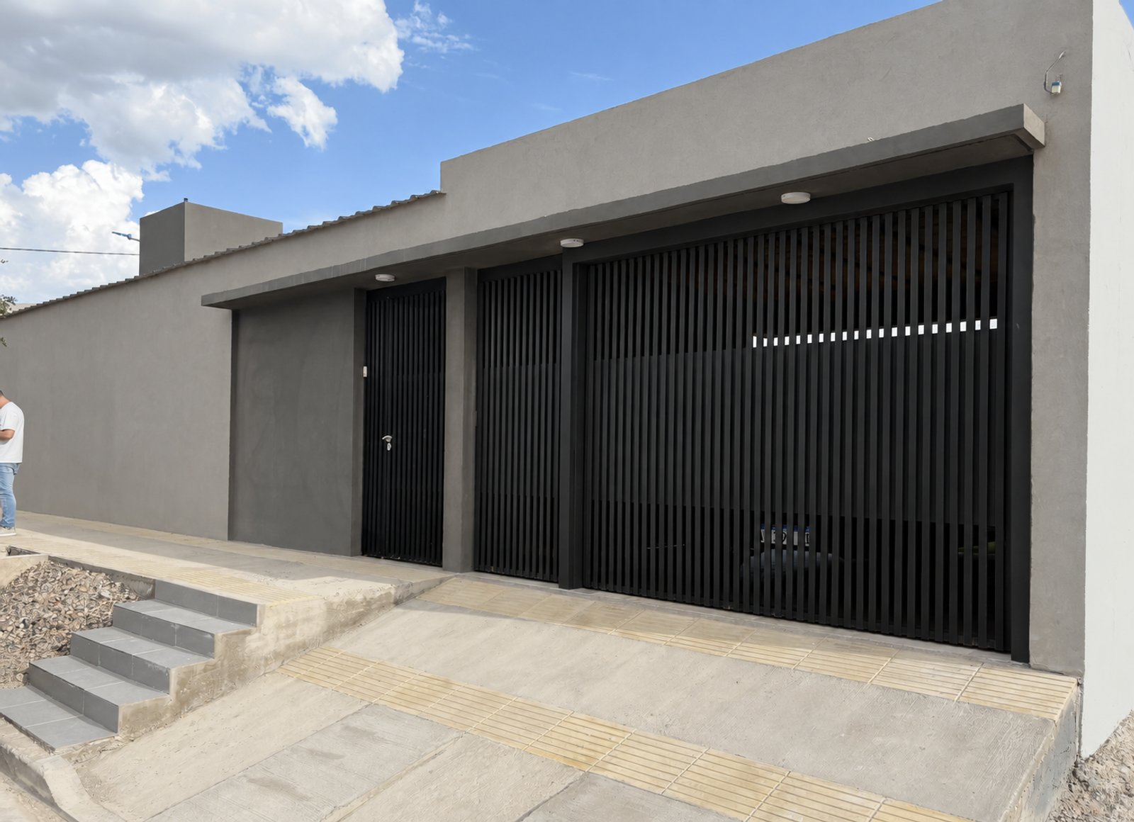 Fachada moderna con portón metálico negro y escaleras de hormigón — proyecto Casa AJ, por Pedro Vilchez, en Neuquén
