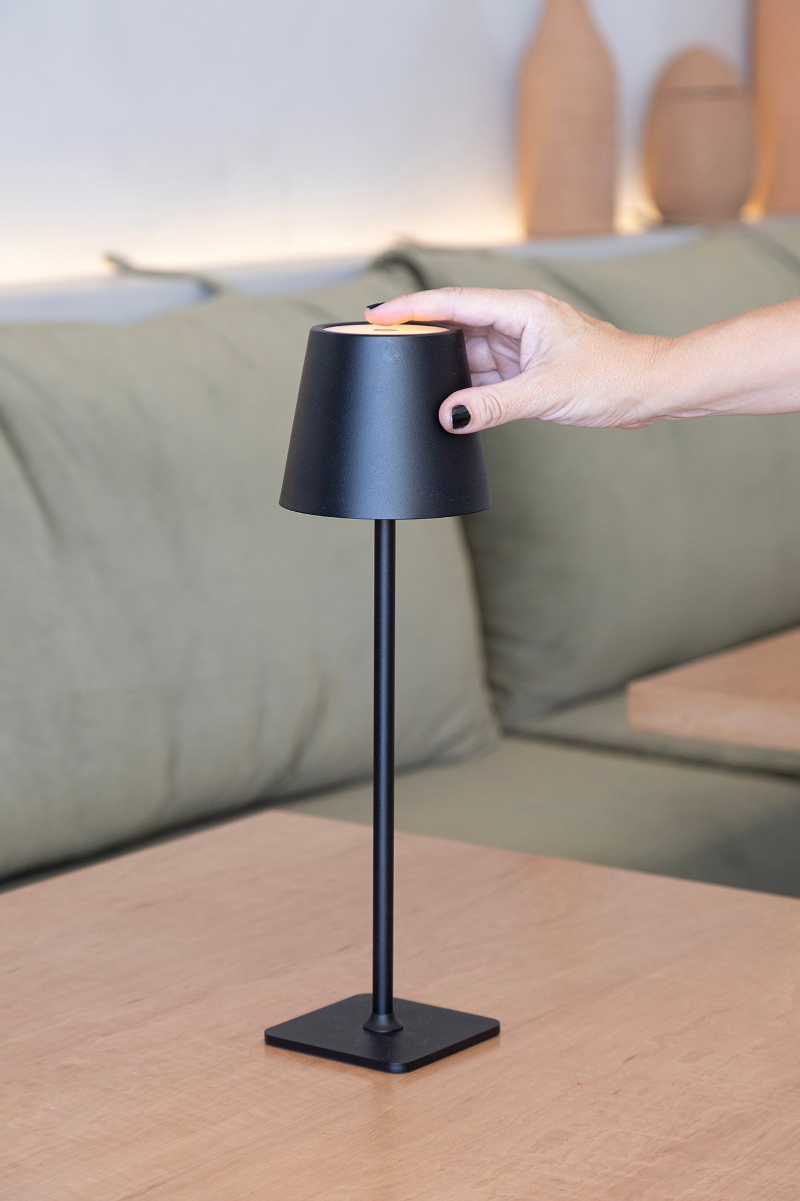 Lámpara de mesa negra moderna sobre mesa de madera con sofá verde al fondo — proyecto HATSU Núñez - MZV Arquitectura, por Gaby Alfonso, en Buenos Aires