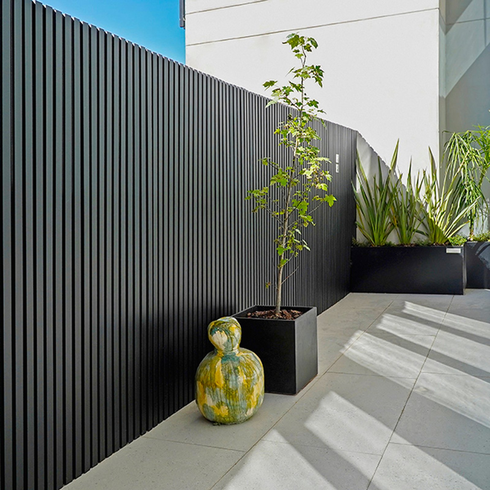 Patio moderno con rejas de metal negro y escultura — proyecto Revestimiento de Aluminio, por Aluar División Elaborados