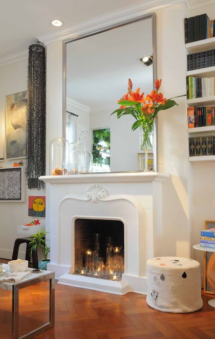 Living moderno con hogar blanco, espejo grande y flores naranjas — proyecto Santa Fe, por Estudio Diez Muzzio, en CABA