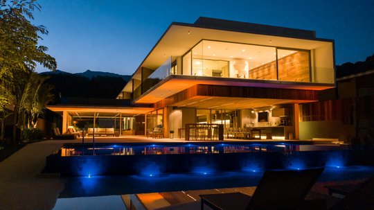 Casa moderna nocturna con pileta iluminada en azul y fachada de vidrio — proyecto Casa Nort, por Toledo Arquitetura E Design