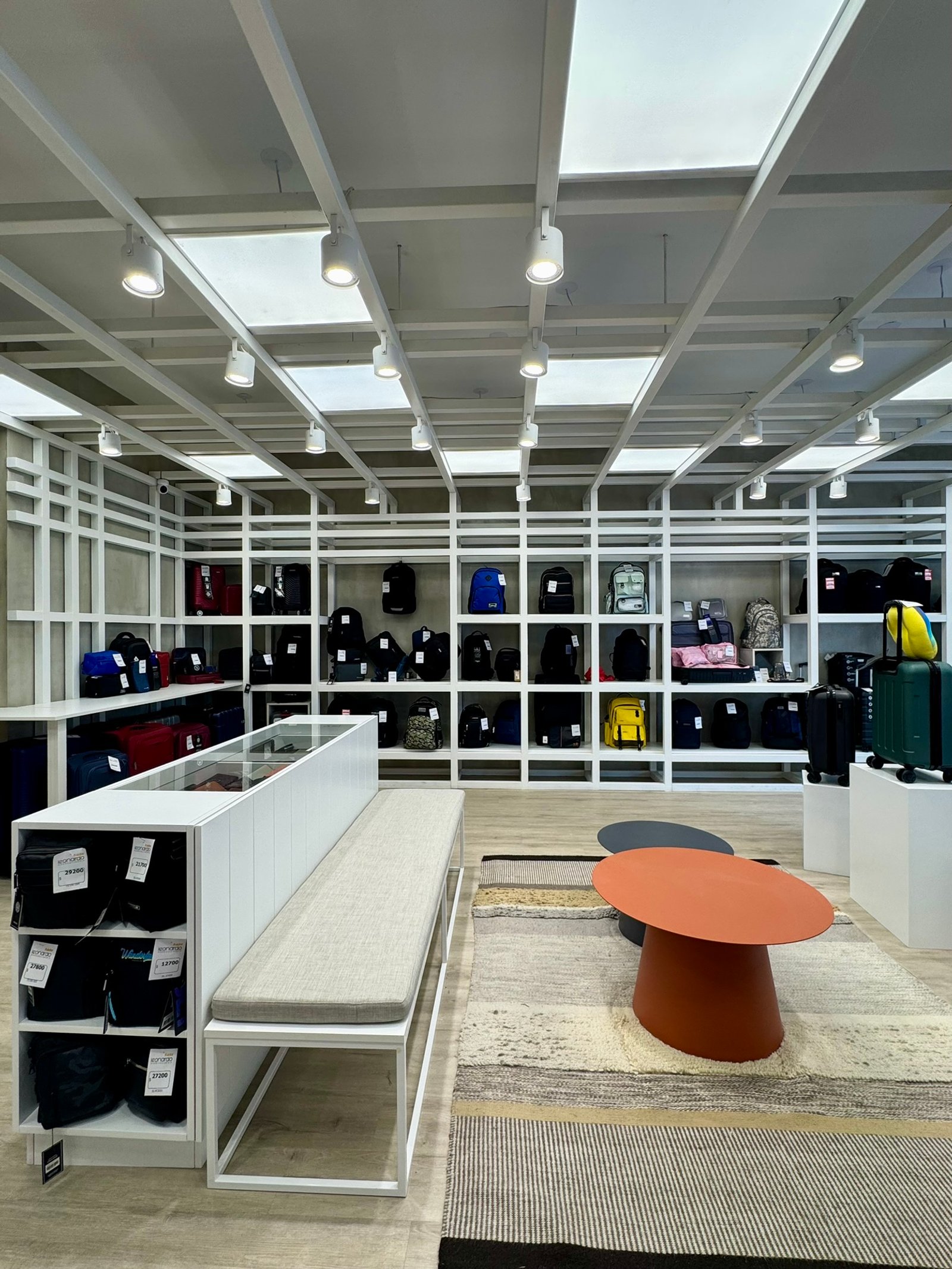 Loja moderna com prateleiras modulares, banco e mesa redonda — projeto Leonardo Marroquinería, por MDBK Arquitectura, em Balvanera