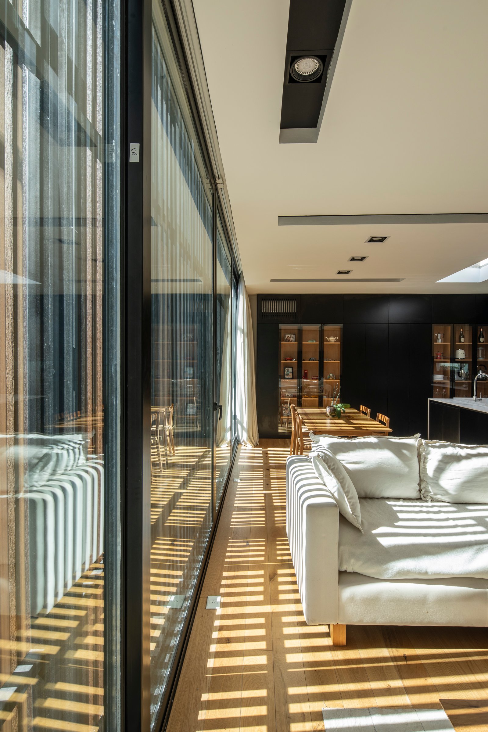 Living moderno con ventanales, luz y sombra sobre piso de madera — proyecto Casa MECHA, por Grupo CRBN, en B1712 Castelar