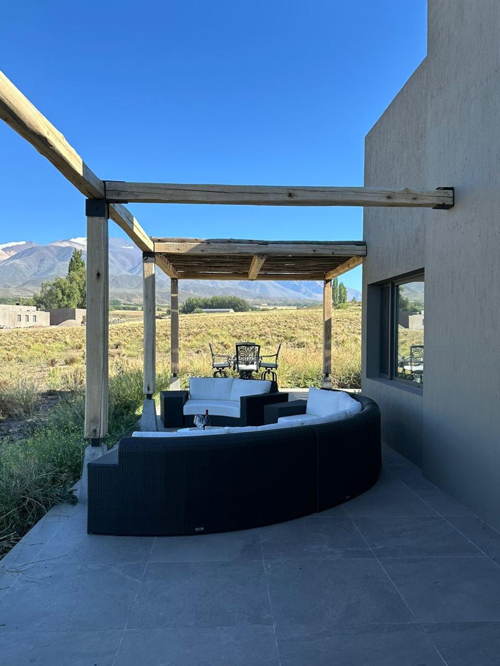 Patio curvo moderno con sofá modular, montañas de fondo y pérgola — proyecto Juegos de Livings Amplios, por Casa Nuñez