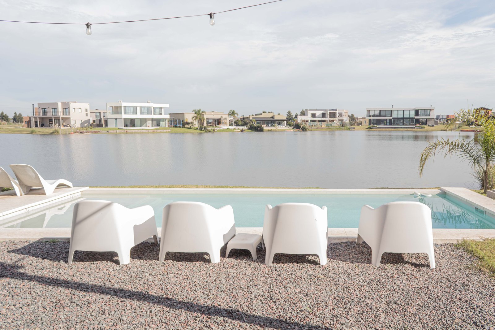 Área de piscina moderna com espreguiçadeiras brancas e vista para o lago — projeto San Sebastian I, por Catalina Fitero Fotografìa, em M472+28