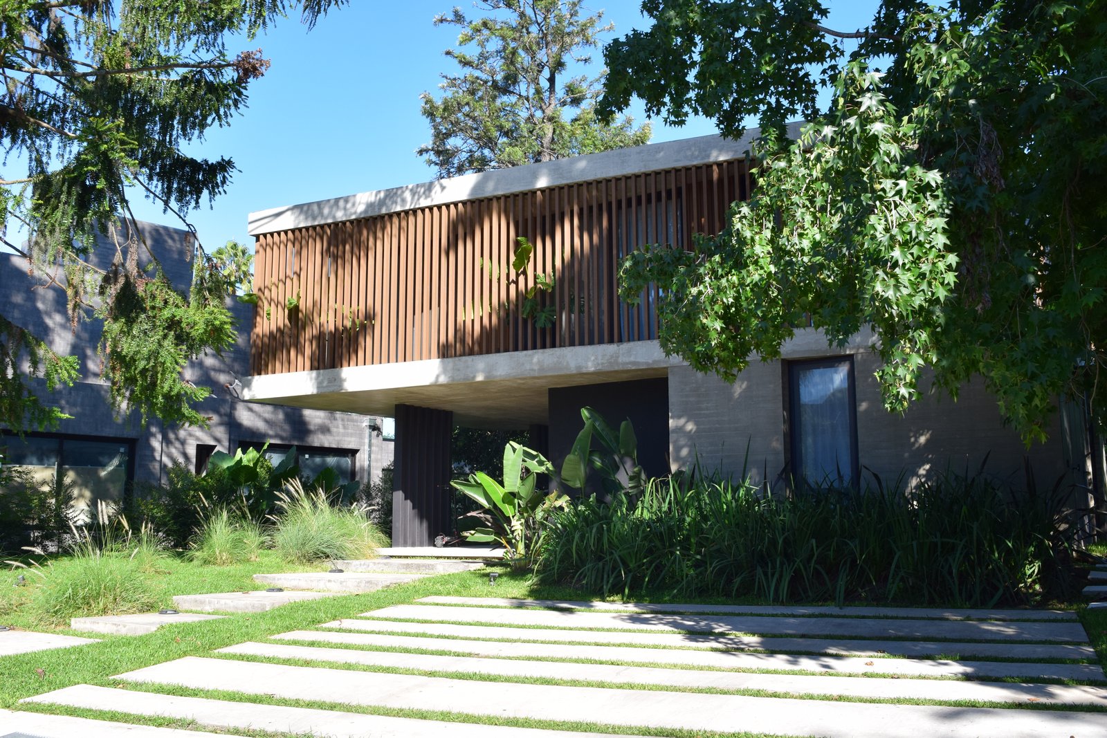 Fachada moderna de concreto y madera con vegetación exuberante — proyecto Obra Highland Park, por lifecycle, en Pilar