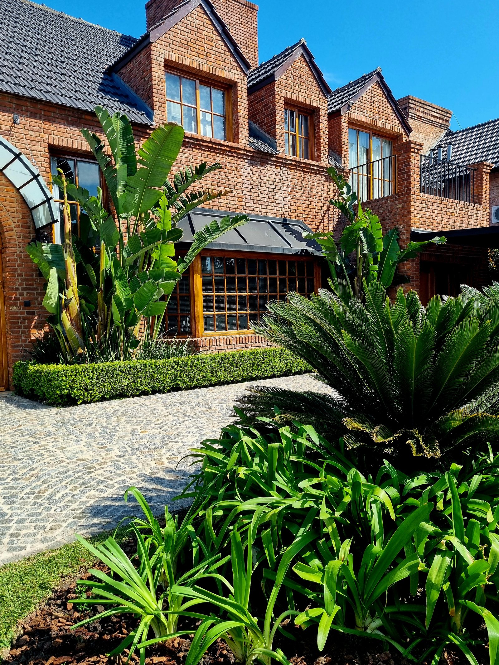 Fachada moderna con ladrillos, arcos y vegetación exuberante — proyecto Miraflores, por Marcela García Brünner Paisajista, en Ruta Panamericana KM 37