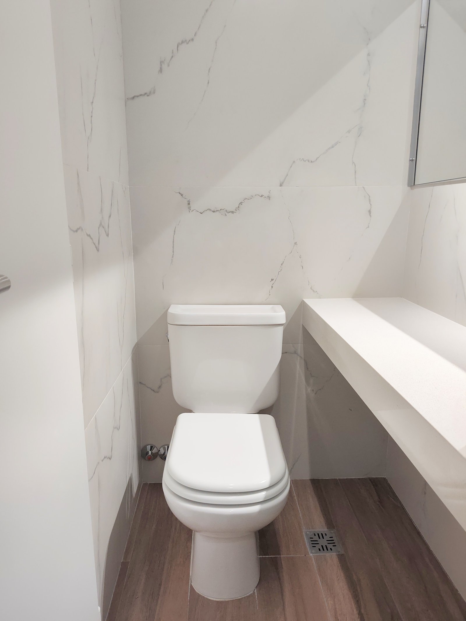 Banheiro moderno com paredes de mármore, piso de madeira e louças brancas — projeto DEPTO 15, por DIKKA Arquitecta, em Avellaneda