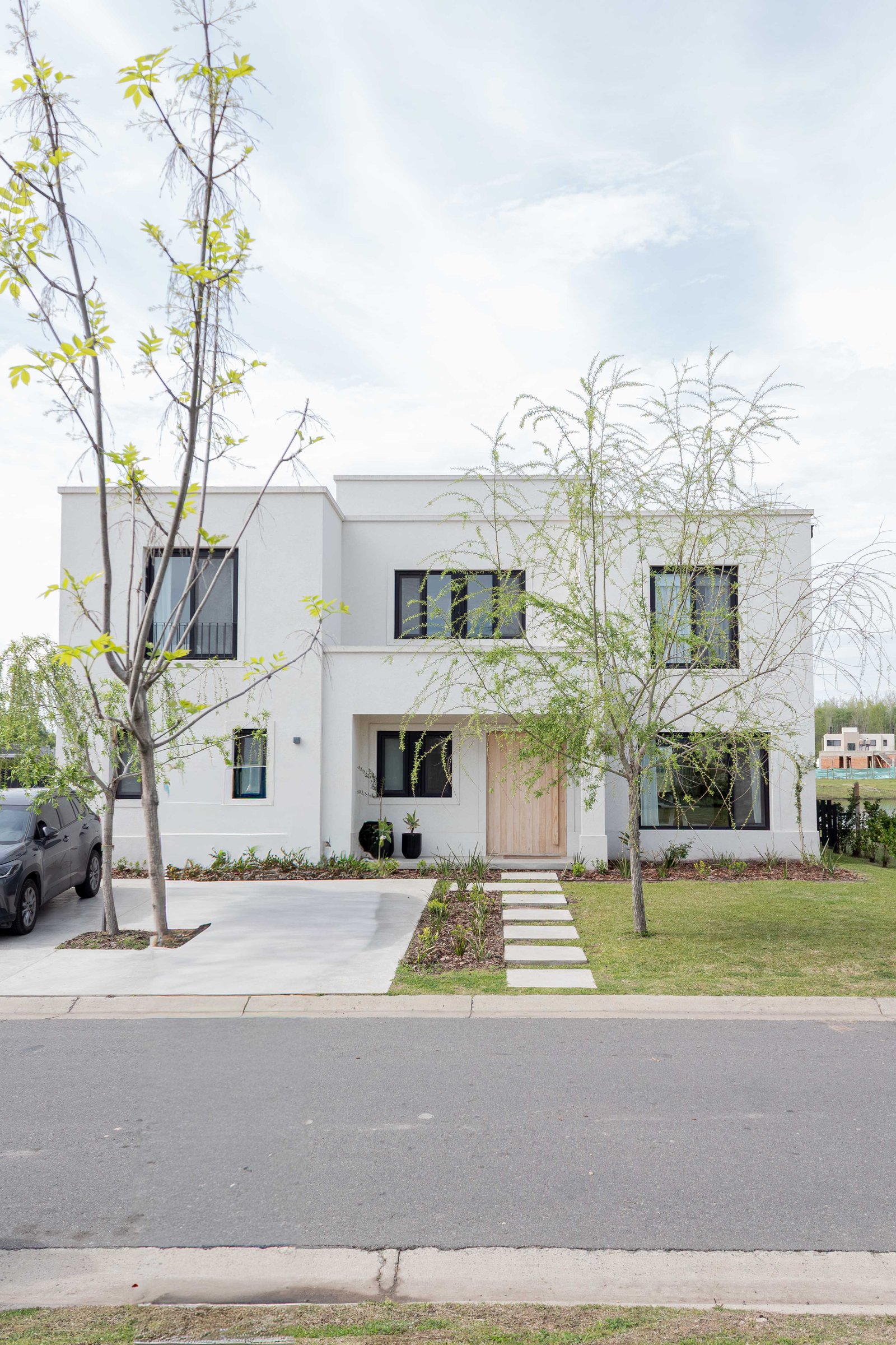 Fachada moderna de casa blanca con grandes ventanales y puerta de madera — proyecto Santa Ana II, por Catalina Fitero Fotografìa, en Arribeños 1611