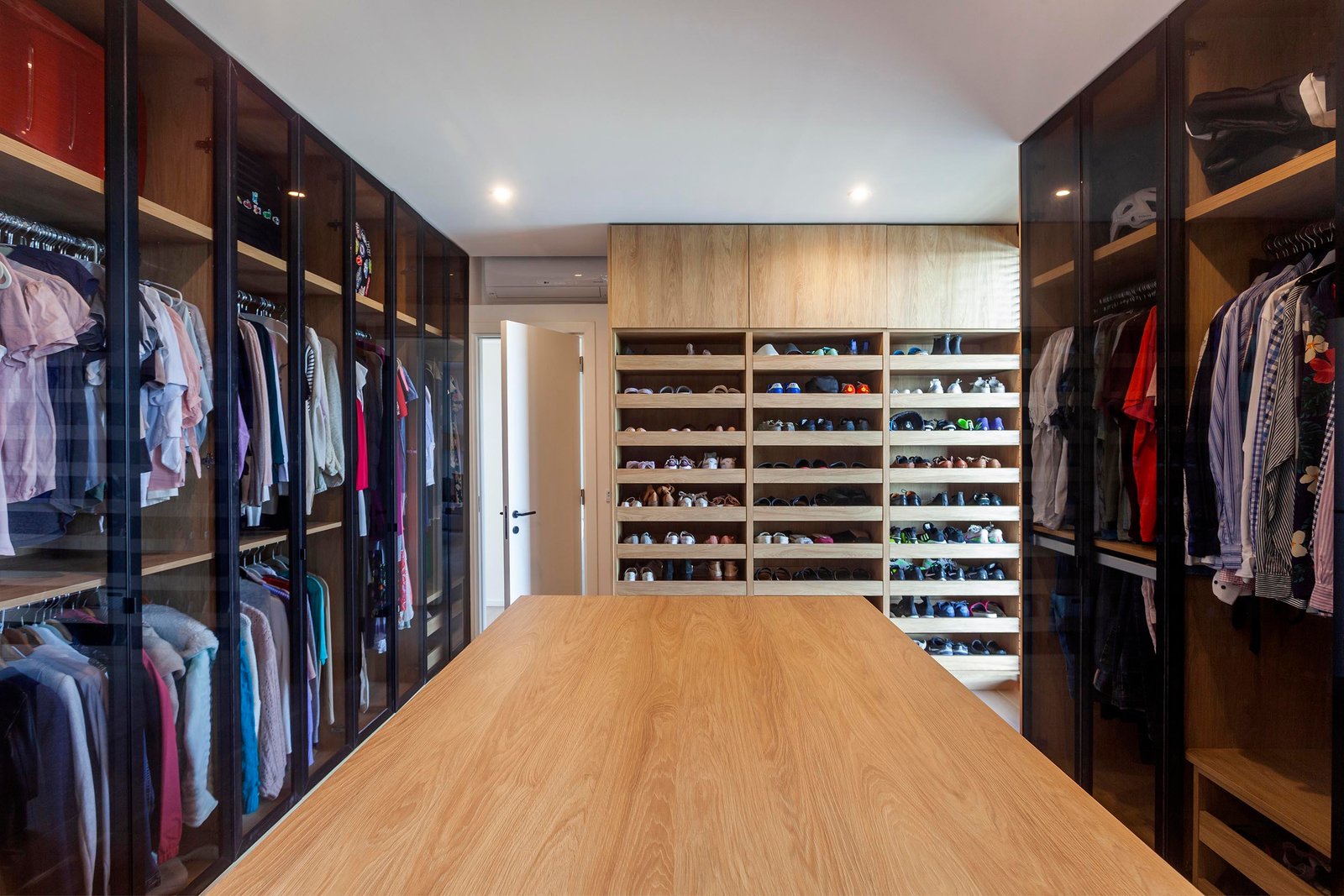 Closet moderno com mesa central de madeira e armários amplos — projeto CASA C313, por A'PRIMA - Arquitectura Sustentable, em Provincia de Buenos Aires