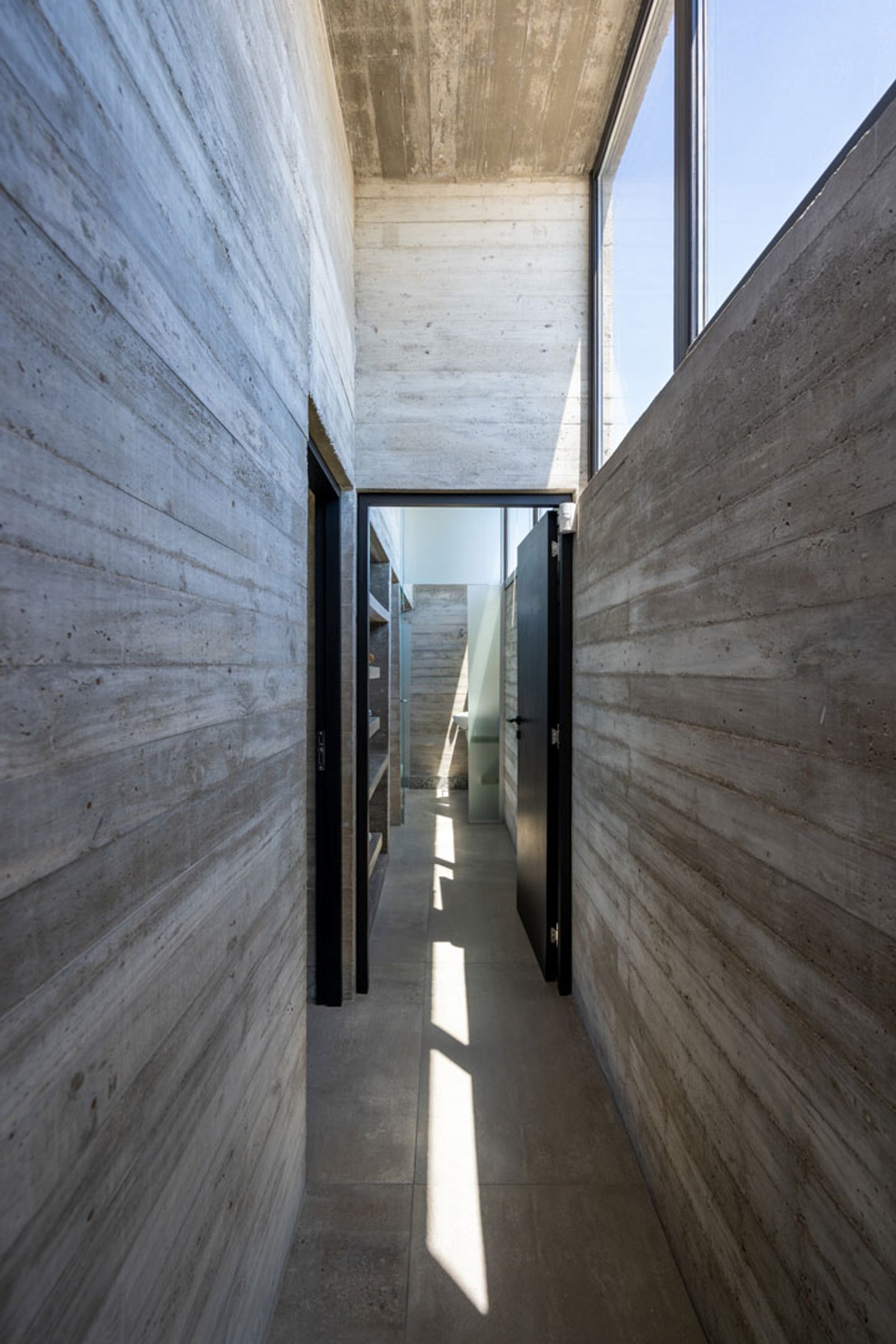 Corredor de concreto aparente, luz natural e design minimalista — projeto Casa La Marina, por Besonías Almeida arquitectos, em X6VF+67