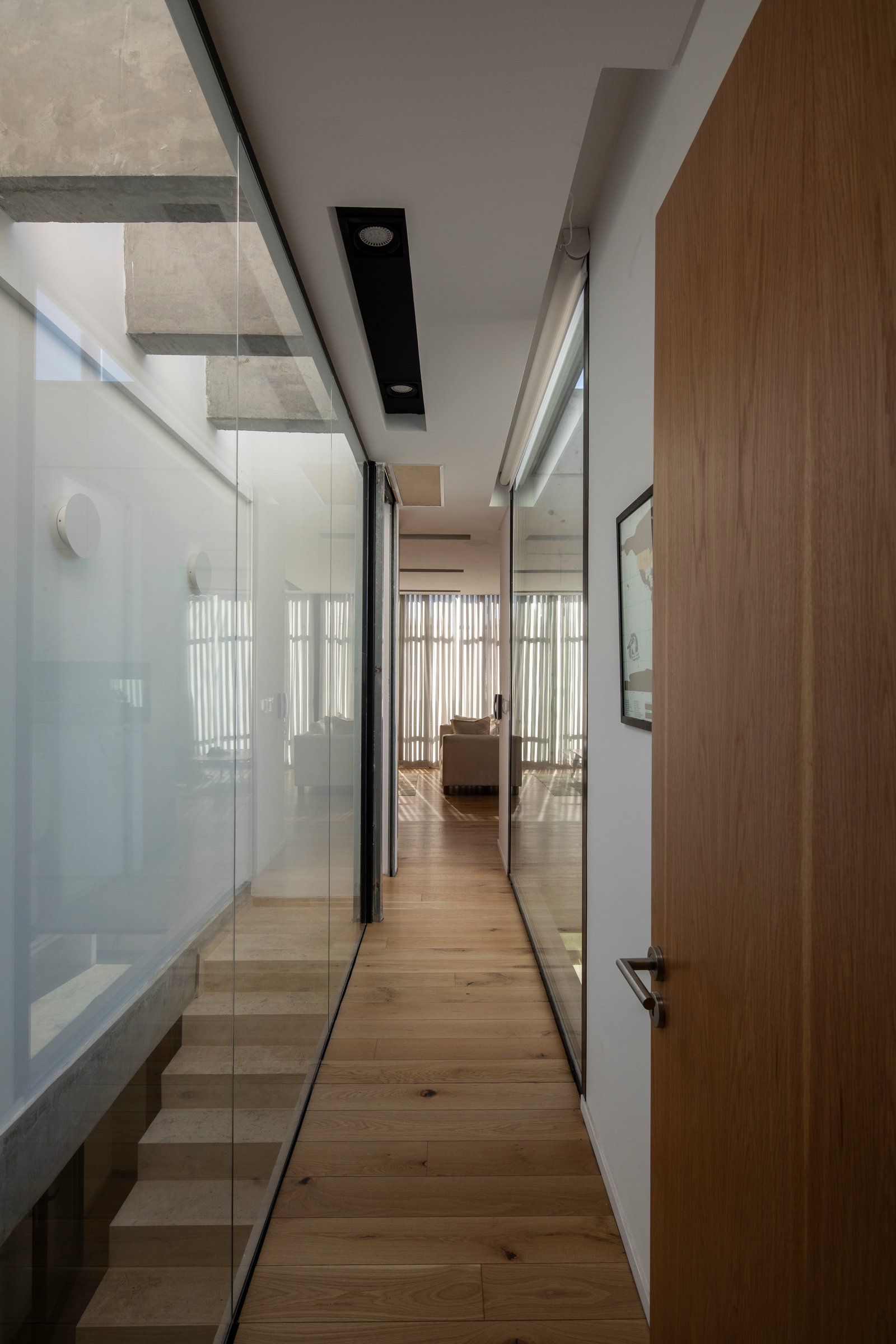Pasillo moderno con escalera flotante y paredes de vidrio — proyecto Casa MECHA, por Grupo CRBN, en B1712 Castelar