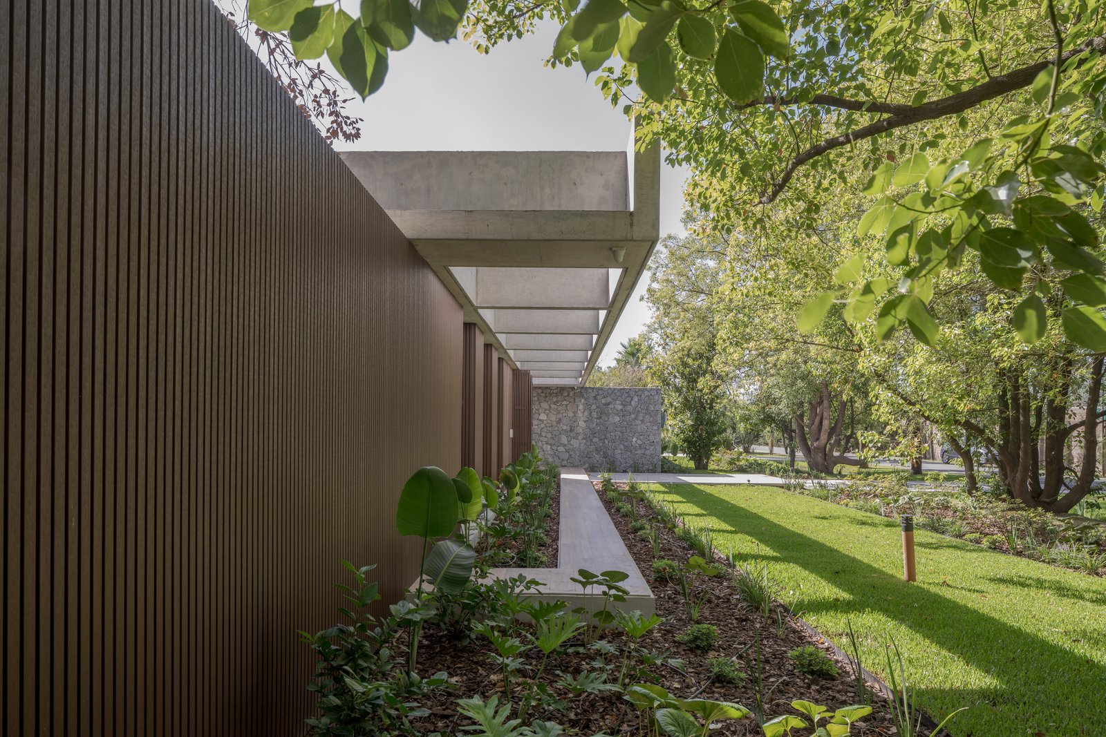 Fachada moderna con pared de madera, pérgola de hormigón y jardín exuberante — proyecto Casa PLANALTO, por Grupo CRBN, en Av. Pres. Perón 10298