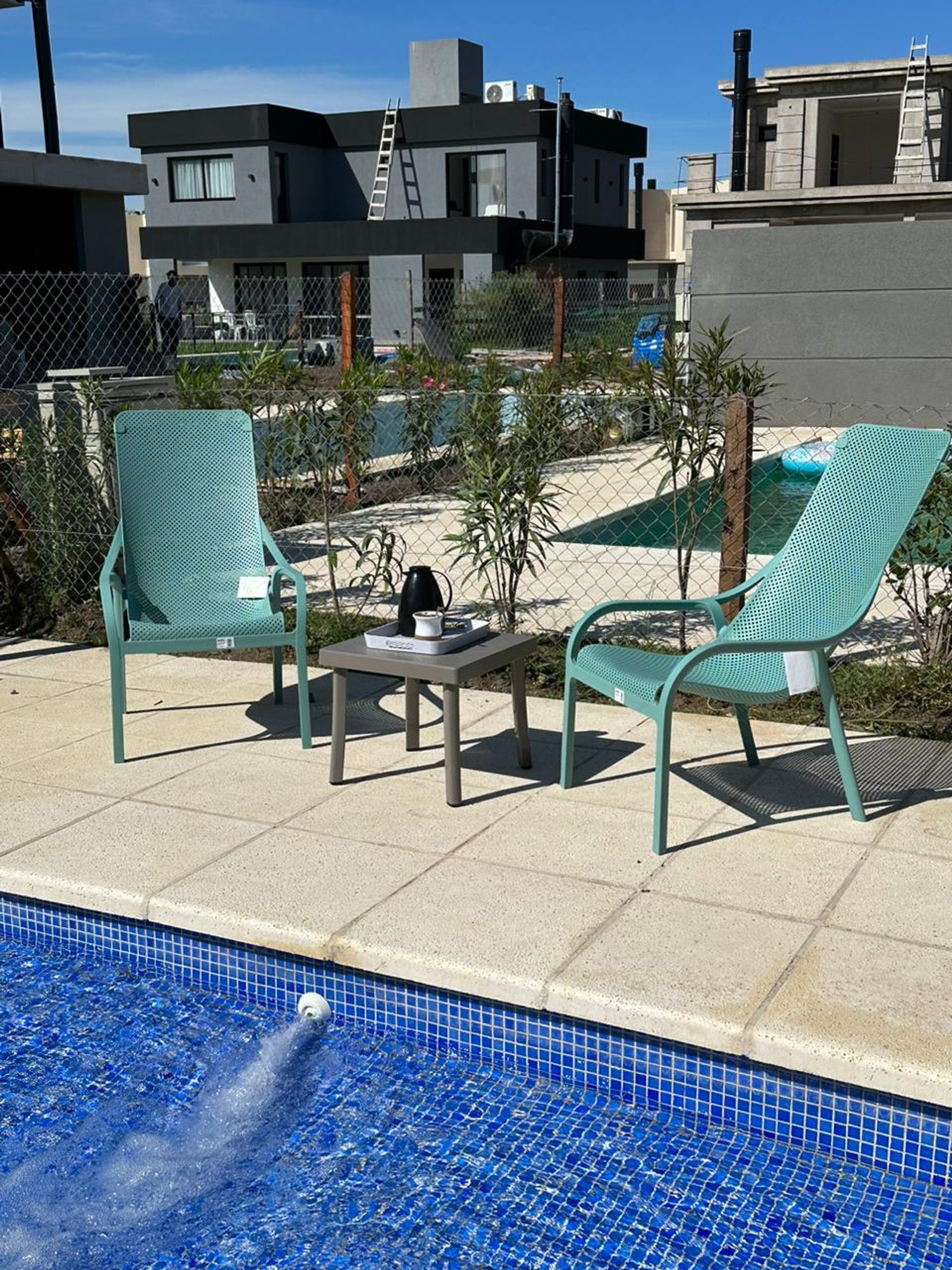 Dos sillas de metal turquesa junto a una piscina moderna — proyecto Reposeras NARDI®, por Casa Nuñez