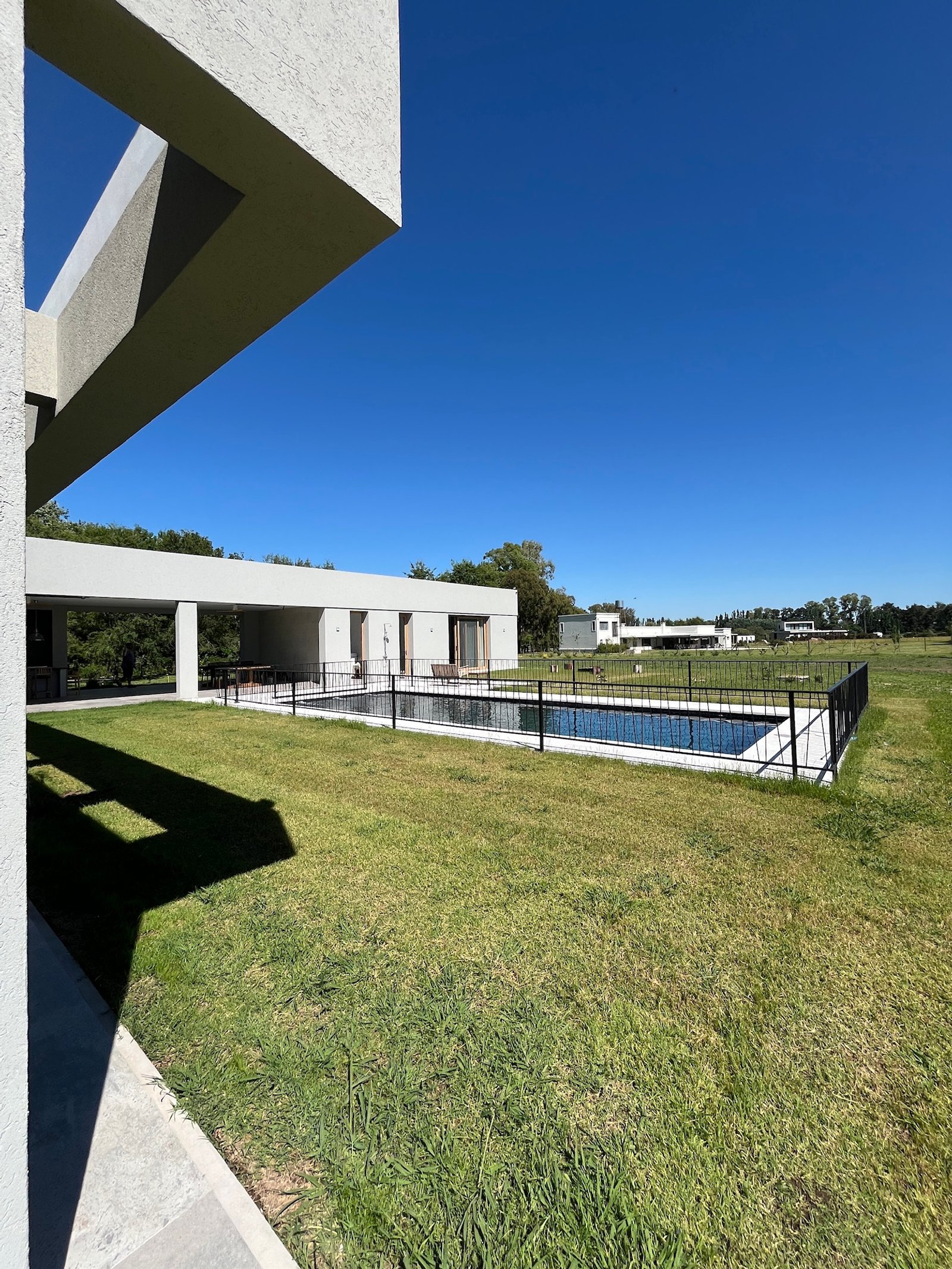 piscina moderna rodeada de césped y valla negra — proyecto La Colina, por Arcucci Arquitectura, en La Colina Villa de Campo