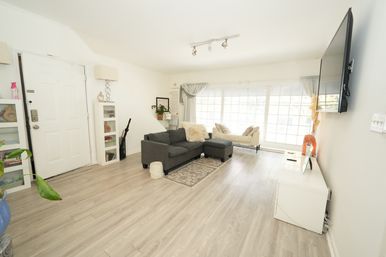 Sunlit modern living room with gray sectional sofa and chaise, light wood floors, large paneled windows and wall-mounted TV