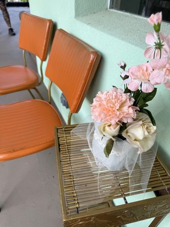 Vintage orange vinyl chairs against a mint-green wall with a gold side table holding a pink carnation and white rose arrangement wrapped in tulle
