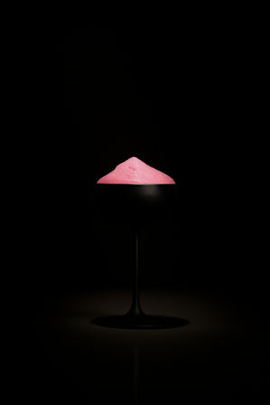 Minimalist cocktail: matte black coupe glass on a dark background topped with a vibrant pink foam mound